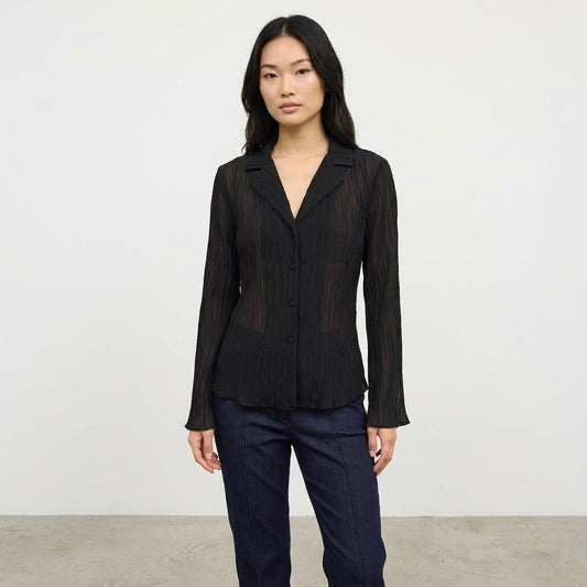 Person in a black blouse and blue jeans against a plain background.