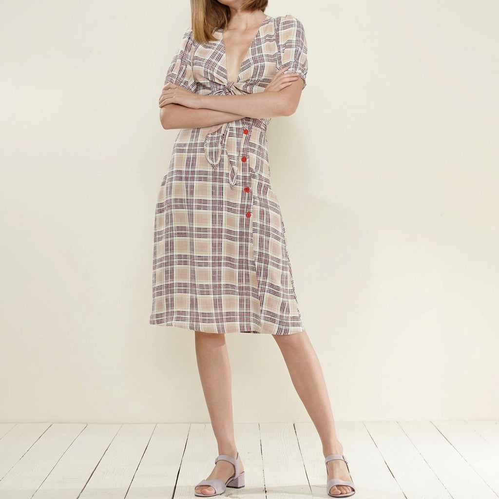 Woman in plaid dress with folded arms, standing on light wooden floor.