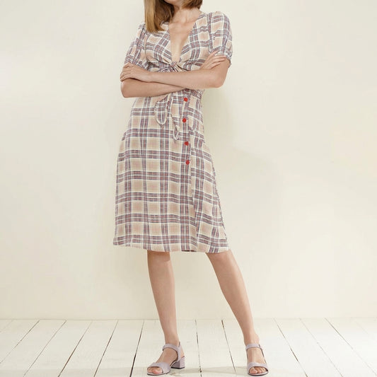 Woman in plaid dress with folded arms, standing on light wooden floor.