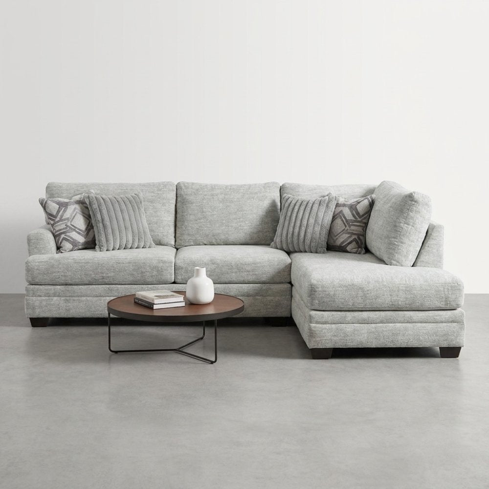Gray sectional sofa with pillows and round coffee table in a minimalist setting.