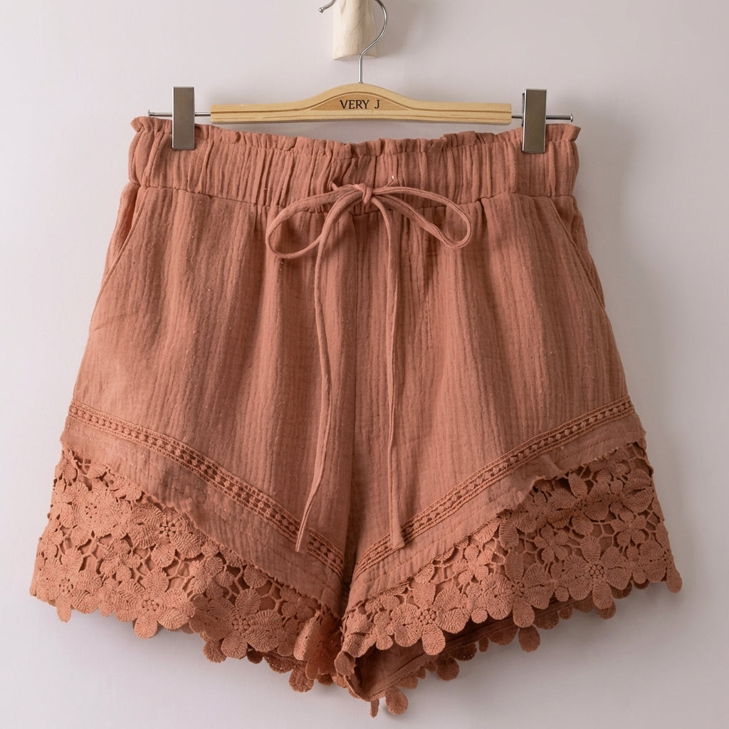 Brown shorts with decorative lace hem on a hanger.
