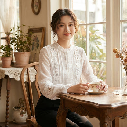 Woman in elegant white blouse enjoying tea by a sunny window.