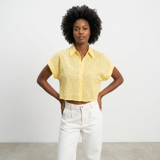 Person in yellow cropped top and white pants standing confidently.