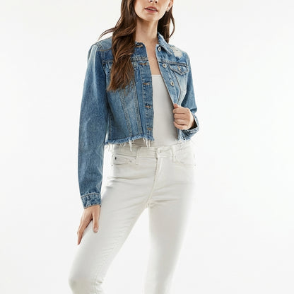 Smiling woman in denim jacket standing outdoors with cafe lights.