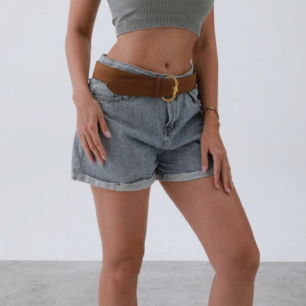 Woman in crop top and denim shorts with a brown belt.
