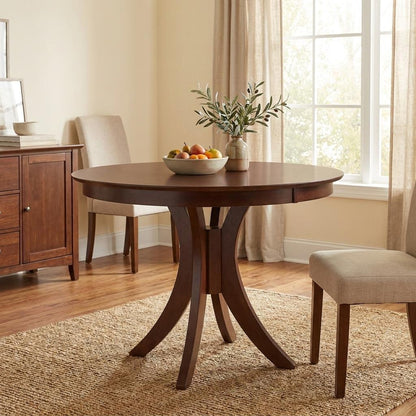 Round wood table with fruit bowl, vase, chairs, and sunlit window.