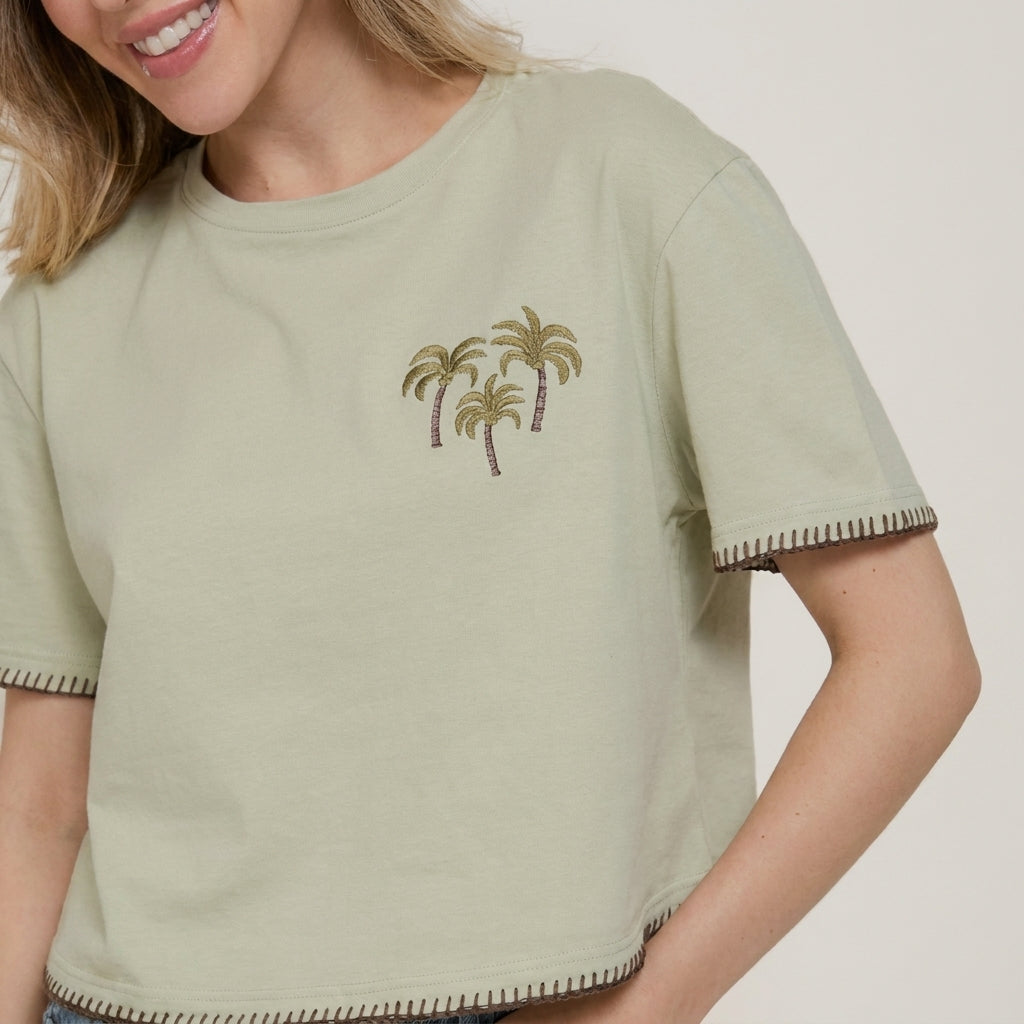 Woman in cropped tee with palm tree design, smiling.