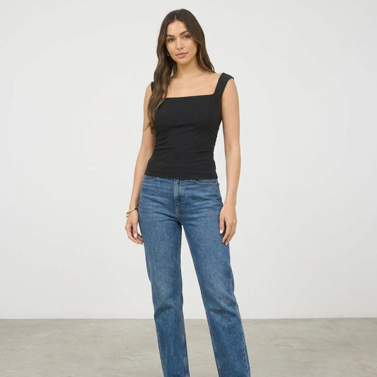Woman in a black top and jeans stands against a plain background.