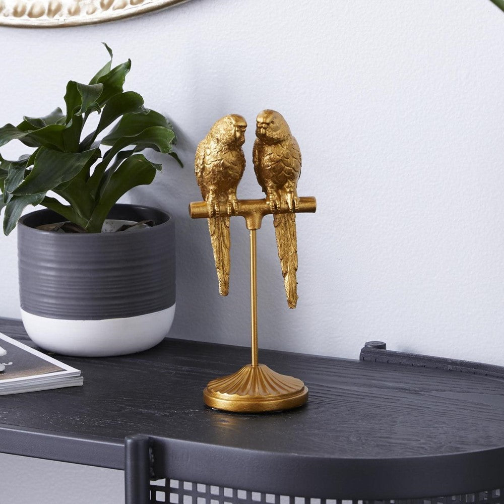 Gold parrot figurines on stand, next to a potted plant on a table.