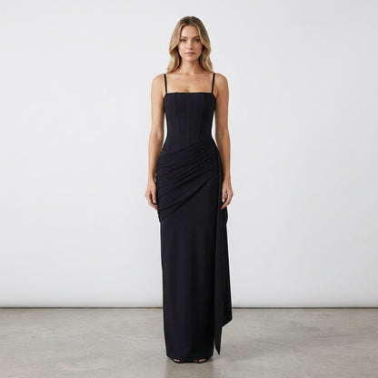 Woman in a sleek black dress with spaghetti straps, posing against a plain background.
