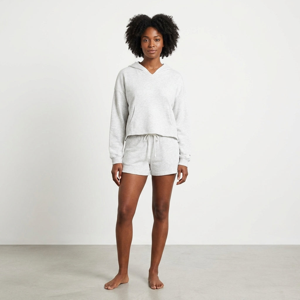 Person in a grey hoodie and shorts stands barefoot on a plain background.
