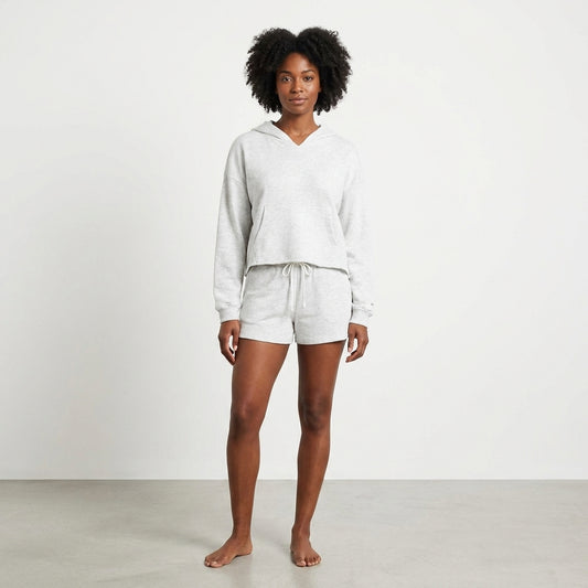 Person in a grey hoodie and shorts stands barefoot on a plain background.