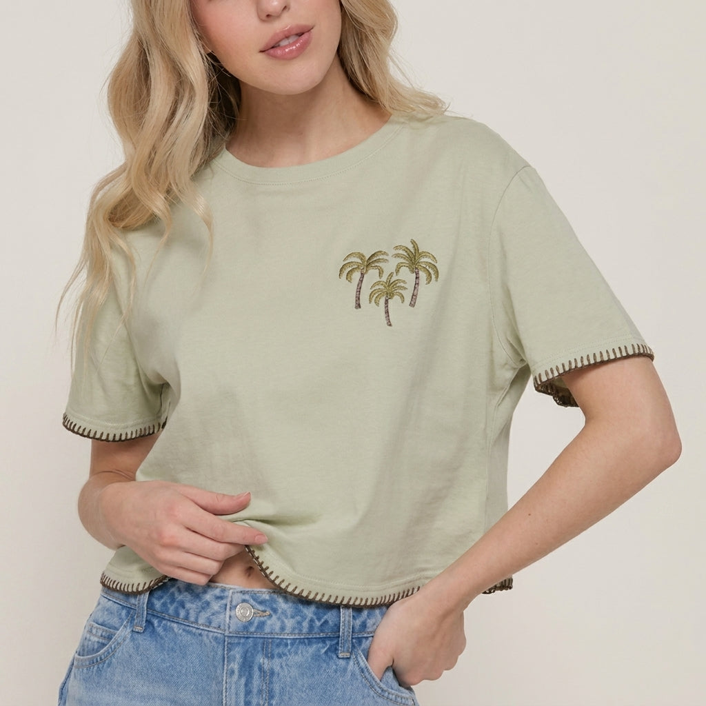 Woman in green tee with palm tree print, light blue jeans.