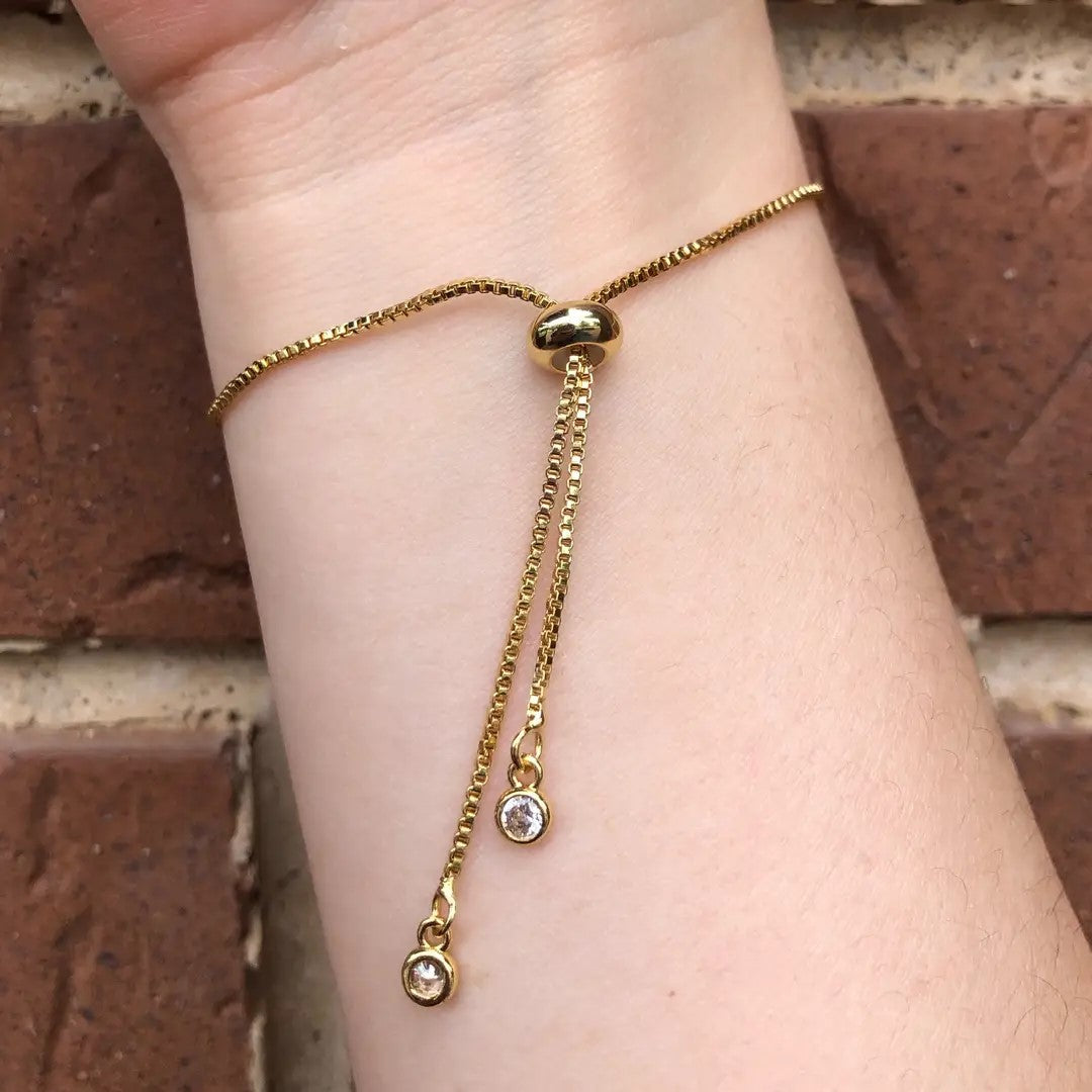 Gold sliding bracelet with dangling jewels, against a brick wall background.