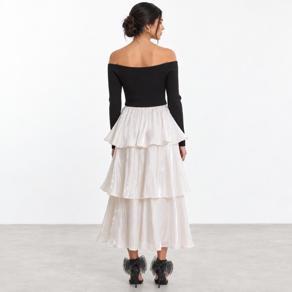 A woman models a black off-shoulder top, tiered white skirt, and black heels.