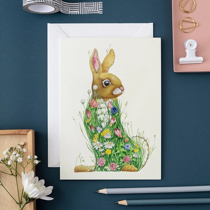 Floral rabbit card on a blue desk with pencils and craft items.