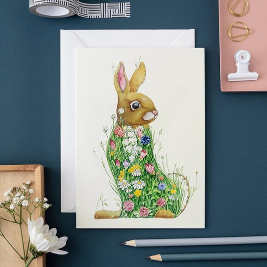 Floral rabbit card on a blue desk with pencils and craft items.