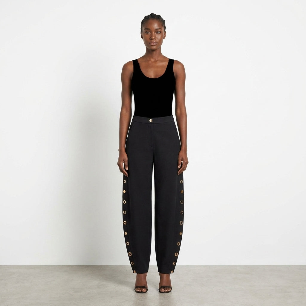 Model in black attire with pants featuring side button details.