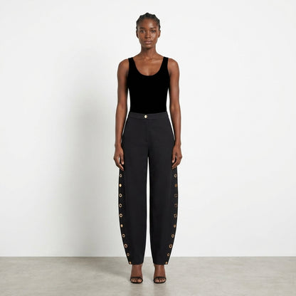 Model in black attire with pants featuring side button details.
