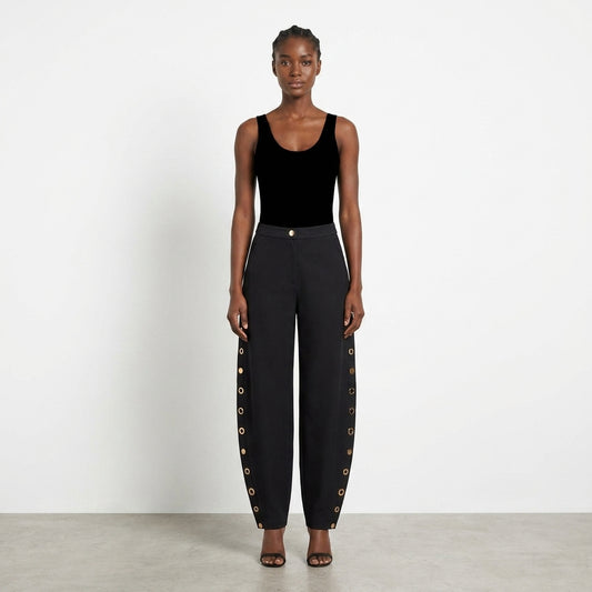 Model in black attire with pants featuring side button details.