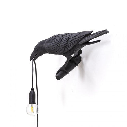 Black crow sculpture holding a hanging light bulb.