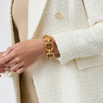 Close-up of a gold chain-link bracelet worn with a white textured tweed blazer.