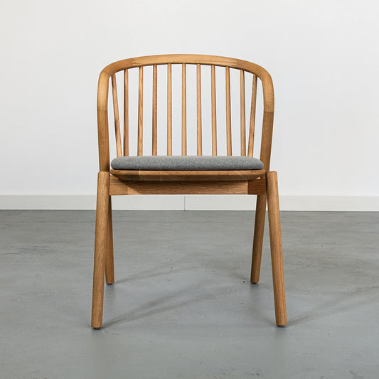 Wooden chair with a gray cushion on a concrete floor.