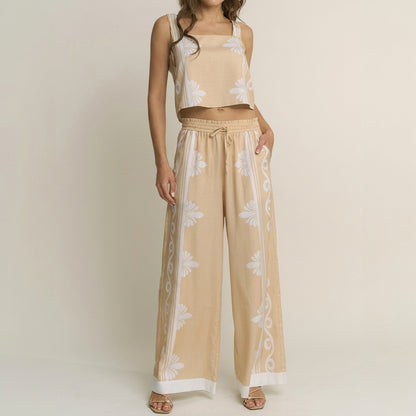 Woman in beige floral-patterned crop top and pants set, standing with hand on hip.