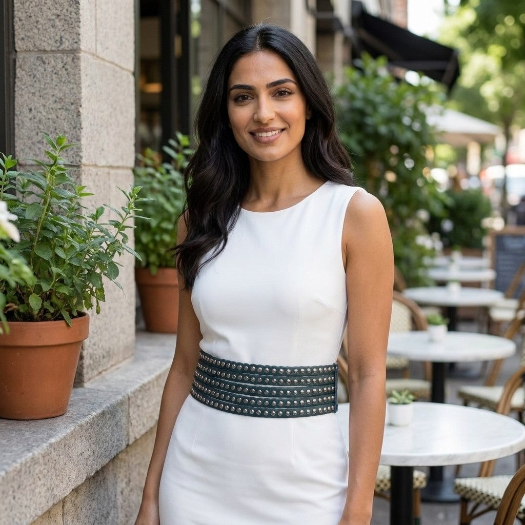 Woman in a white dress smiling outdoors beside cafe tables and potted plants.