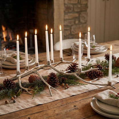 Lit candles on a festive table with pinecones and greenery.