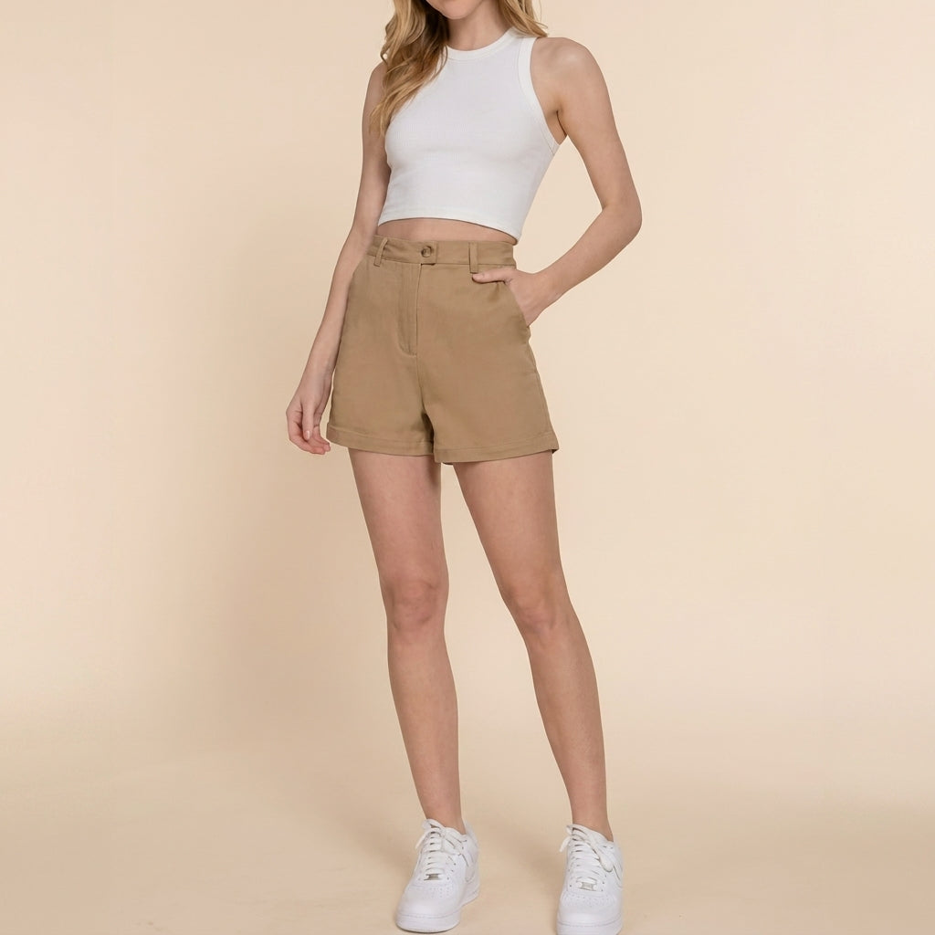 Person in white crop top, khaki shorts, and sneakers on a beige background.