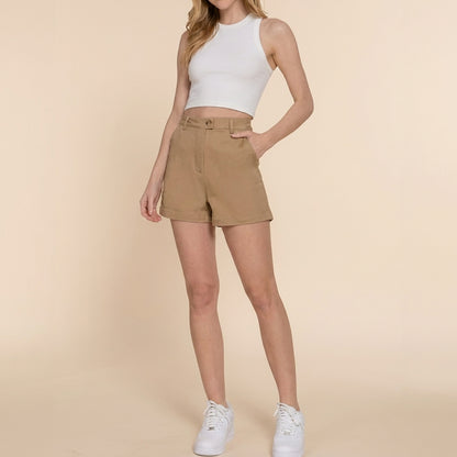 Person in white crop top, khaki shorts, and sneakers on a beige background.