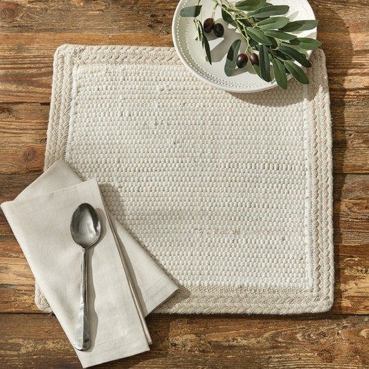 Woven mat with napkin, spoon, and olive decor on rustic wooden table.