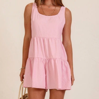 Woman wearing a pink sleeveless dress holding a straw bag.