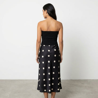 Woman in a black strapless top and polka dot skirt, facing away.