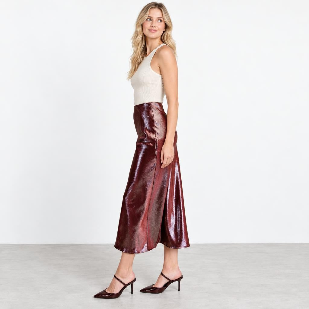 A woman models a glossy burgundy midi skirt, white tank top, and matching heels.