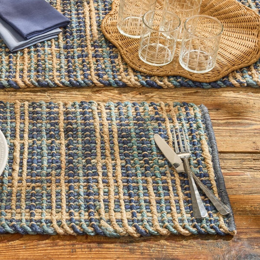 Woven placemats, cutlery, and glasses on a rustic wooden table.