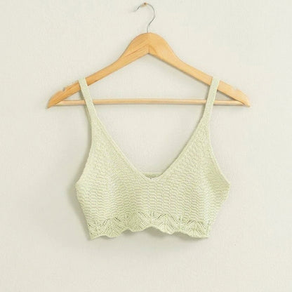 Knitted crop top on a wooden hanger against a white wall.