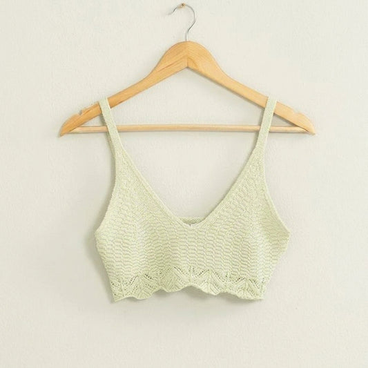 Knitted crop top on a wooden hanger against a white wall.
