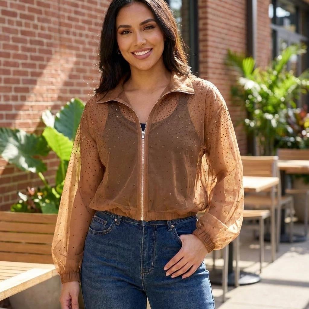 Woman in sheer brown jacket and jeans, smiling outdoors.