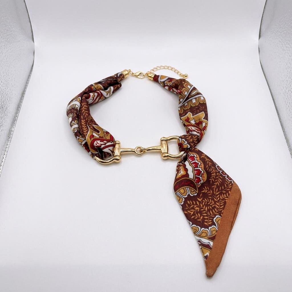 A patterned brown fabric bracelet with gold-tone hardware displayed on a white background.