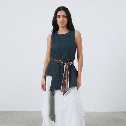 Woman in blue sleeveless top, white skirt, and belt with scarf.