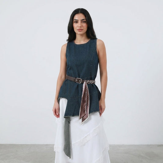 Woman in blue sleeveless top, white skirt, and belt with scarf.