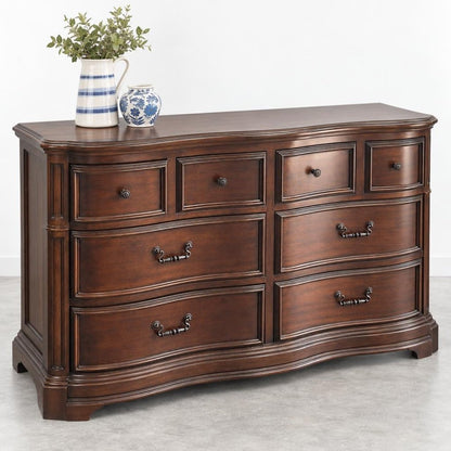 Wooden dresser with curved drawers, decorated with vases and a plant on top.