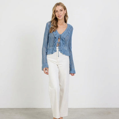 Woman in blue crochet top and white pants, standing against a white background.