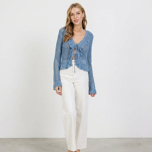 Woman in blue crochet top and white pants, standing against a white background.