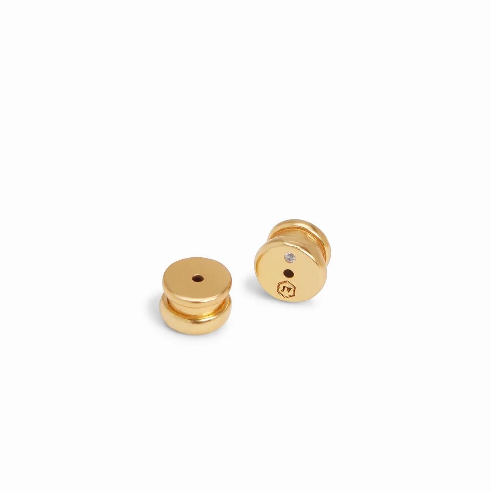 Two small gold-colored metal fasteners, one showing a tiny clear stone and engraved emblem.