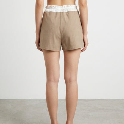 Person wearing beige pinstripe shorts with a white waistband, seen from the back.