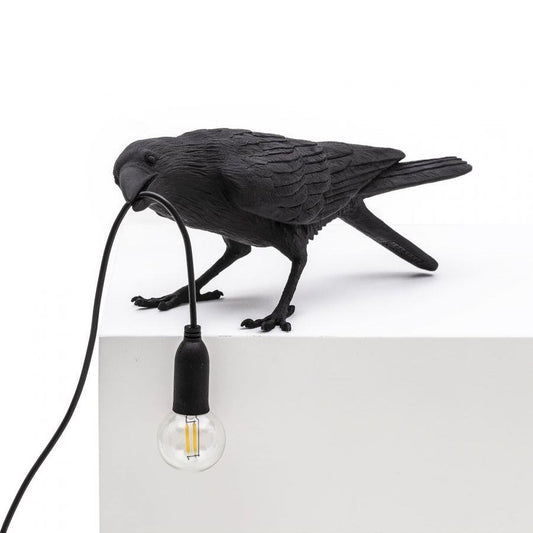 Crow sculpture holding a light bulb with its beak.