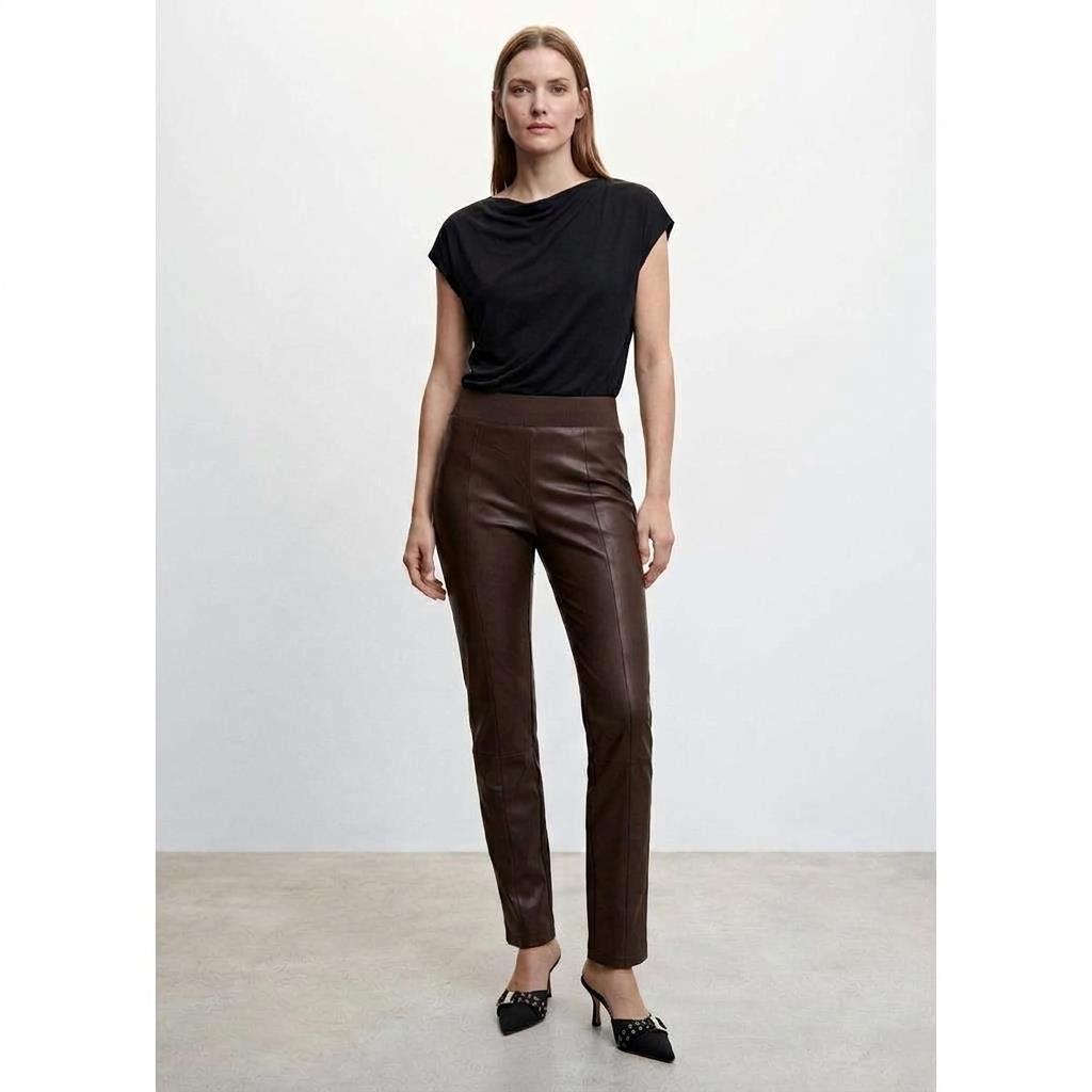 Woman in black top and leather pants, standing confidently.